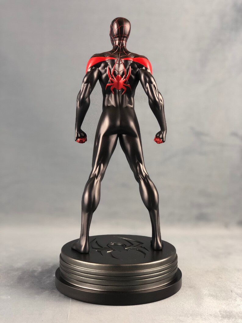 May include: Black and red Spider-Man action figure standing on a black base with a spider logo. The figure is posed with its arms raised and fists clenched.