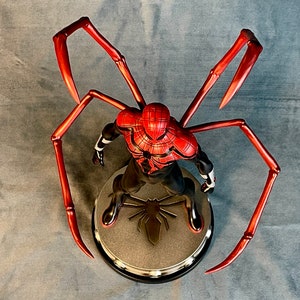 May include: A red and black Spider-Man action figure with long, red, spindly legs. The figure is posed in a standing position with its arms outstretched. The figure is standing on a black base with a spider logo.