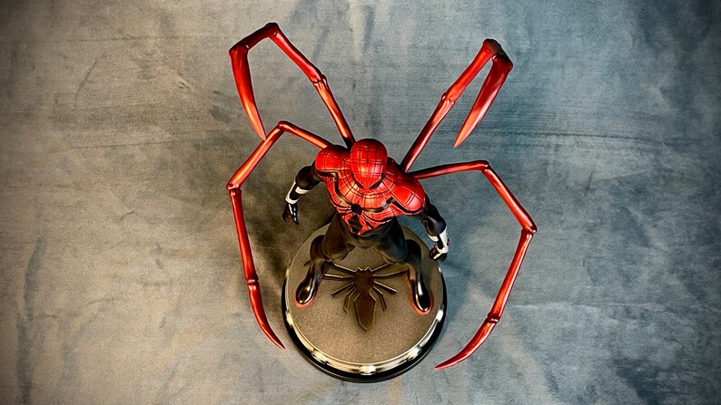 May include: A red and black Spider-Man action figure with long, red, spindly legs. The figure is posed in a standing position with its arms outstretched. The figure is standing on a black base with a spider logo.