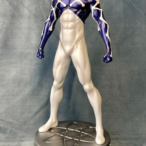 Puede incluir: Una figura de acci&oacute;n blanca y azul de un superh&eacute;roe con una m&aacute;scara roja y blanca. La figura est&aacute; de pie sobre una base plateada con un s&iacute;mbolo de &aacute;tomo estilizado.