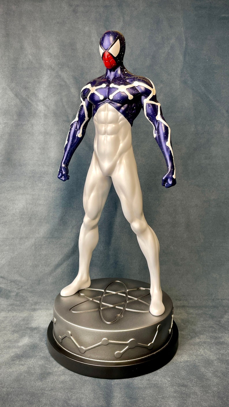 Puede incluir: Una figura de acci&oacute;n blanca y azul de un superh&eacute;roe con una m&aacute;scara roja y blanca. La figura est&aacute; de pie sobre una base plateada con un s&iacute;mbolo de &aacute;tomo estilizado.