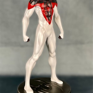 May include: A white and red action figure of Spider-Man with a black spider symbol on his chest. The figure is standing on a round, metallic base with a spider symbol.