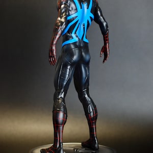 May include: A black and red superhero figure with a blue spider emblem on the back. The figure is standing on a silver circular base. The suit has red web-like detailing and the figure is posed with its back to the viewer.