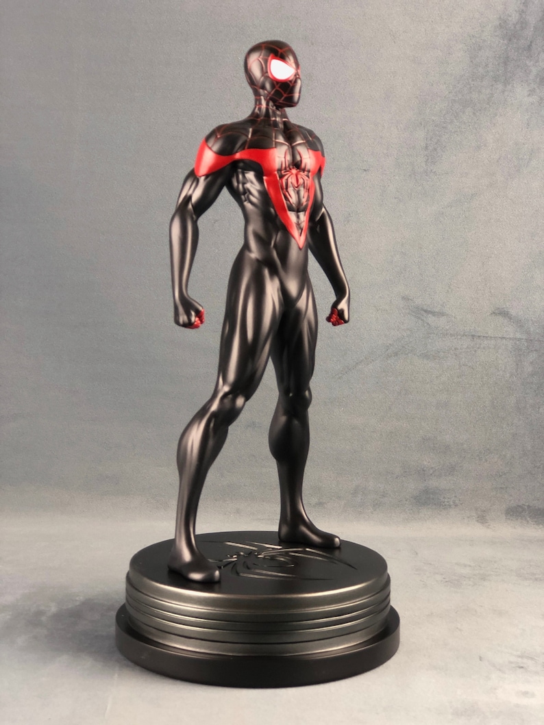 May include: Black and red Spider-Man action figure with a black base. The figure is standing with its arms at its sides and its head turned to the right. The figure is posed in a dynamic stance.