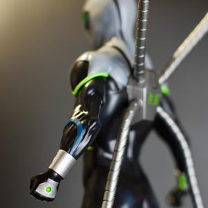 Puede incluir: Una figura de acci&oacute;n negra y plateada de un superh&eacute;roe con cuatro brazos mec&aacute;nicos. La figura tiene ojos verdes brillantes y un detalle azul y plateado en el brazo.