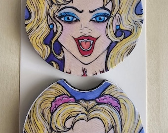 May include: Two circular car coasters featuring a graphic illustration of a blonde character with blue eyeshadow, blue earrings, and fangs. The coasters are displayed on a white card labelled Car Coasters Handmade with love.
