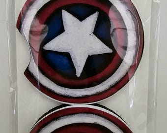 May include: Two car coasters with a Captain America shield design. Each coaster features a white star on a blue background, surrounded by red and white concentric circles. The packaging reads "Car Coasters" and "Handmade with love."