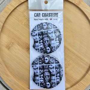 May include: Two black and white car coasters with a graphic print of a collage of faces. The coasters are packaged in a clear plastic bag with a white header that reads "CAR COASTERS hand made with love".