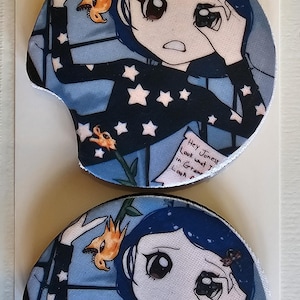May include: Two car coasters featuring a cartoon character with blue hair and a black top with white stars. The coasters have a blue background with a floral design and text that reads "Hey Jonesy, Look what I..."