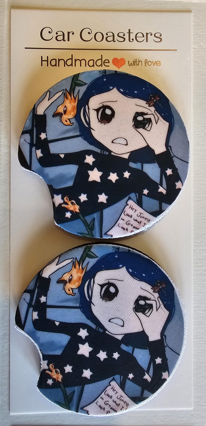 May include: Two car coasters featuring a cartoon character with blue hair and a black top with white stars. The coasters have a blue background with a floral design and text that reads "Hey Jonesy, Look what I..."