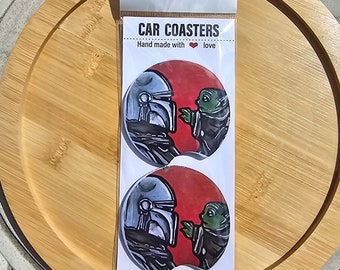 May include: Two round car coasters featuring a cartoon image of a Mandalorian and Grogu, also known as Baby Yoda. The coasters are white with a red background and the text "CAR COASTERS" and "Hand made with love".