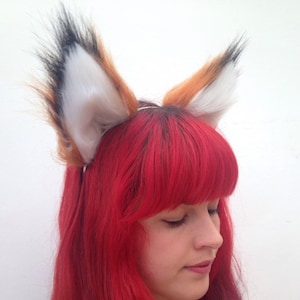 Könnte beinhalten: Eine Person mit langen, rot-violetten Ombre-Haaren trägt ein Stirnband mit Fuchs-Fell-Ohren. Das Stirnband ist braun und weiß mit schwarzen Spitzen.