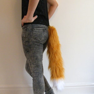 May include: A person wearing denim jeans with a fluffy orange and white fox tail attached to the back of their waistband.
