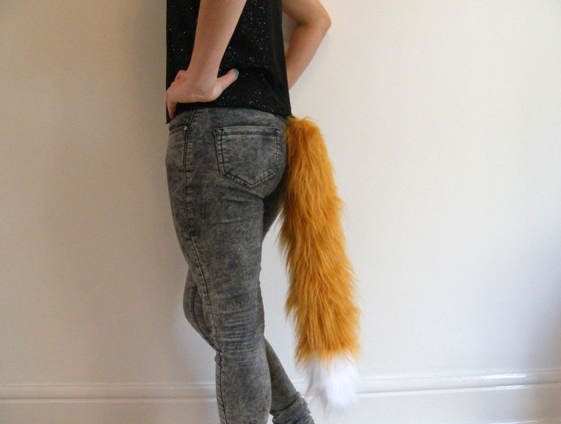 May include: A person wearing denim jeans with a fluffy orange and white fox tail attached to the back of their waistband.