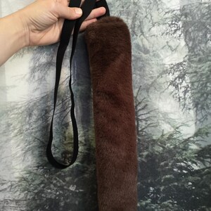 May include: A brown faux fur tail with a black adjustable strap. The tail is long and fluffy, and the strap is made of a durable material.