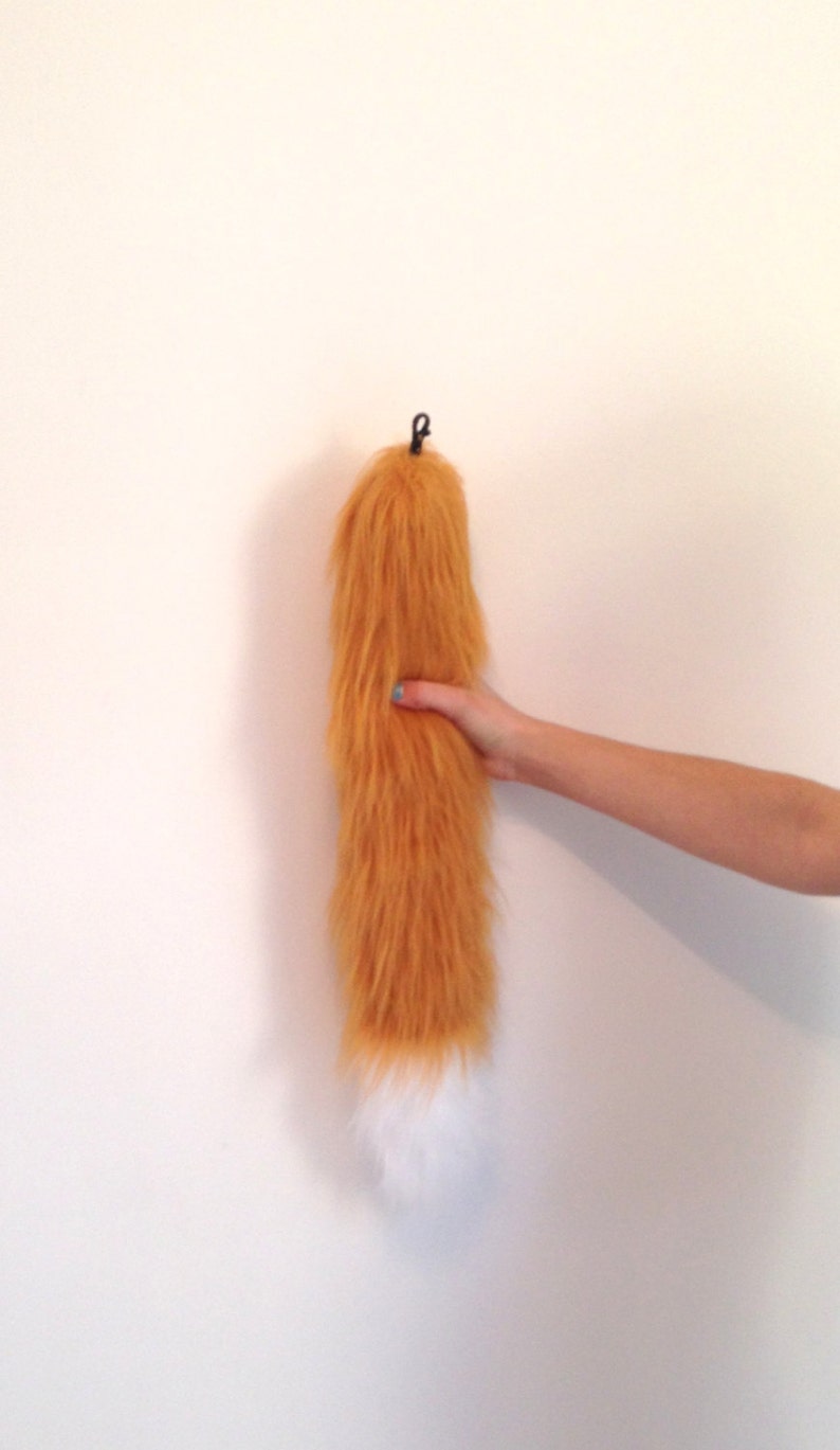 May include: A long, fluffy orange fox tail with a white tip. The tail is attached to a black clip.