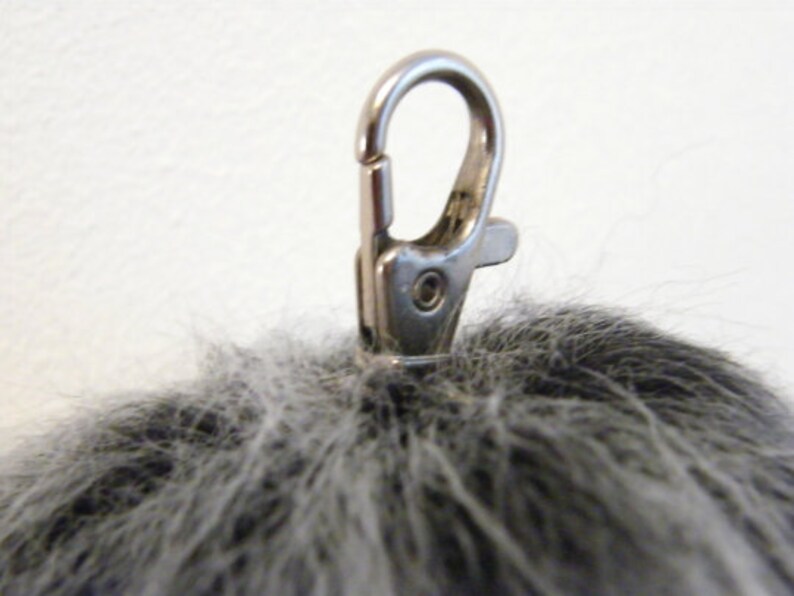 May include: A gray fluffy pom pom keychain with a silver metal clasp.
