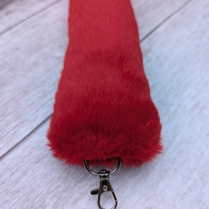 May include: A bright red fluffy tail with a silver metal clip. The tail is made of faux fur and is attached to a keychain.