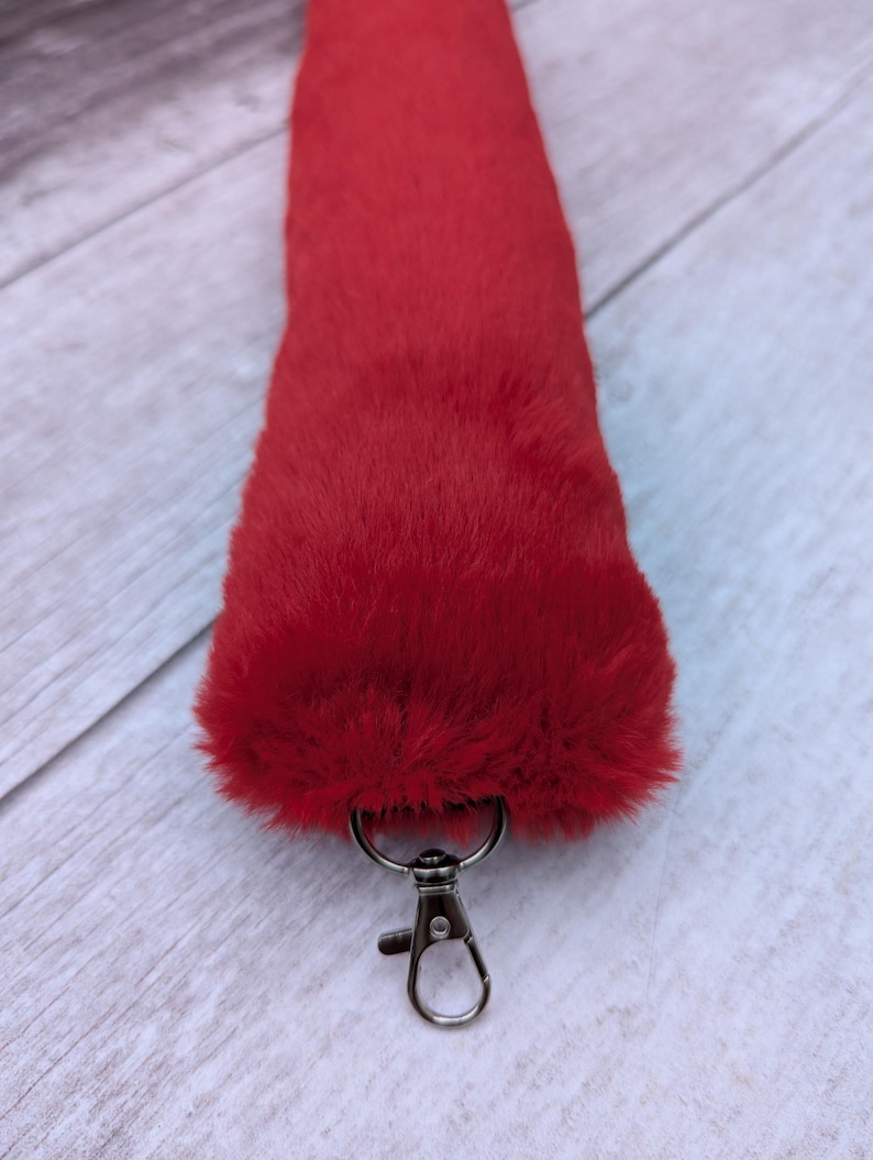 May include: A bright red fluffy tail with a silver metal clip. The tail is made of faux fur and is attached to a keychain.