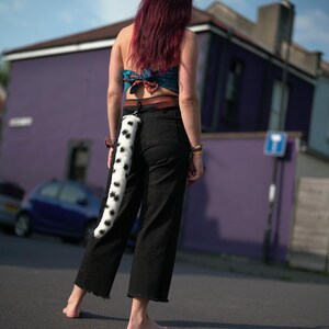 May include: A person wearing black pants and a blue and white patterned top with a black and white spotted tail attached to a belt.