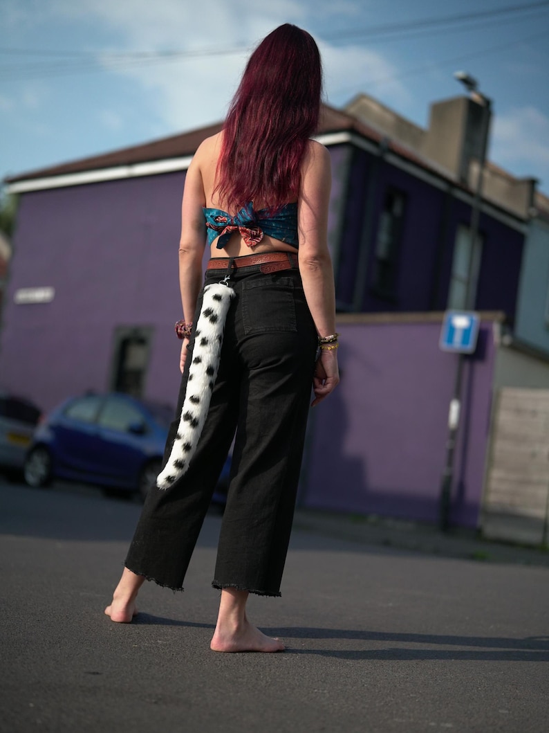 May include: A person wearing black pants and a blue and white patterned top with a black and white spotted tail attached to a belt.