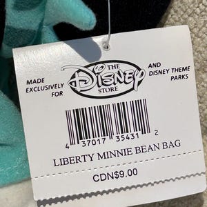 May include: A white tag with black text and a barcode. The tag says "Made Exclusively For The Disney Store" and "And Disney Theme Parks". The tag also says "Liberty Minnie Bean Bag" and "CDN$9.00".