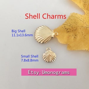 Könnte beinhalten: Zwei goldfarbene Muschel-Anhänger, einer groß und einer klein. Der größere Muschel-Anhänger misst 11,1 x 13,6 mm und der kleinere Muschel-Anhänger misst 7,8 x 8,8 mm. Etsy: Umonograms
