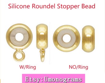 May include: Gold-toned silicone roundel stopper bead with a ring attached. The bead is shown in two views, one with the ring and one without.