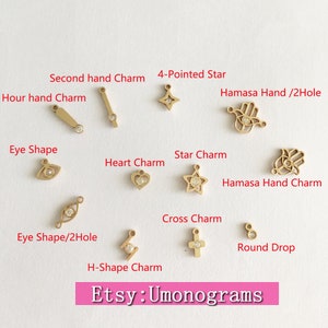 May include: A collection of gold-toned charms with clear crystal accents. The charms include a star, heart, eye, cross, and hand. The text "Etsy: Umonograms" is visible at the bottom of the image.