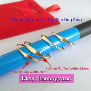 May include: Four gold stacking rings with flat tops, shown on a blue surface. The rings are 1 mm and 1.27 mm wide. The text "1mm/1.27mm Flat Top Stacking Ring" and "Etsy: Umonograms" is visible in the image.