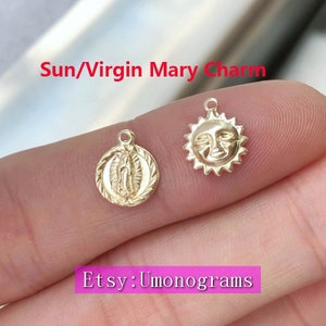 May include: Two gold charms, one depicting the Virgin Mary and the other a sun with a face. The charms are on a finger, with the text "Sun/Virgin Mary Charm" above and "Etsy: Umonograms" below.