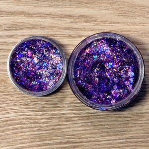 May include: Two clear jars filled with purple and iridescent glitter. The jars are different sizes.