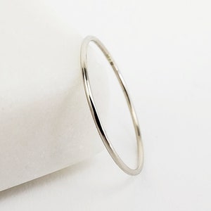 May include: A thin, silver ring. The ring is a simple band design, with a smooth, polished surface. The ring is set against a white background, with a slight shadow adding depth. The ring appears to be made of metal.