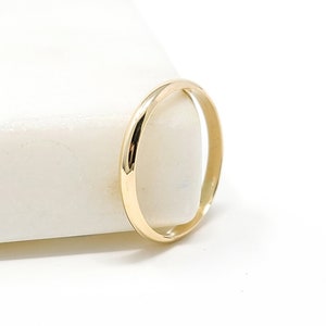 May include: A delicate gold ring with a smooth, rounded band. The ring is set against a white background, highlighting its simple elegance. This minimalist piece is perfect for everyday wear.