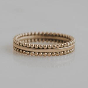 May include: A gold ring with a beaded design. The ring is made of three bands, two with beaded edges and one smooth band in the centre.