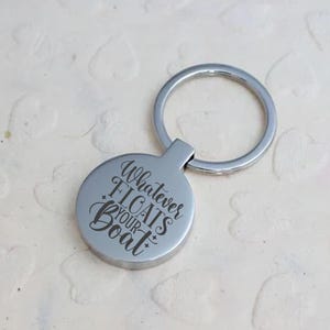 May include: A silver keyring with a circular pendant. The pendant is engraved with the phrase "Whatever Floats Your Boat" in a cursive font. The keyring is attached to the pendant by a small, rectangular piece.