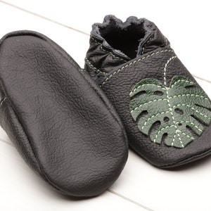 May include: Black leather baby shoes with a green leaf design. The shoes have a soft, flexible sole and are perfect for crawling and walking.