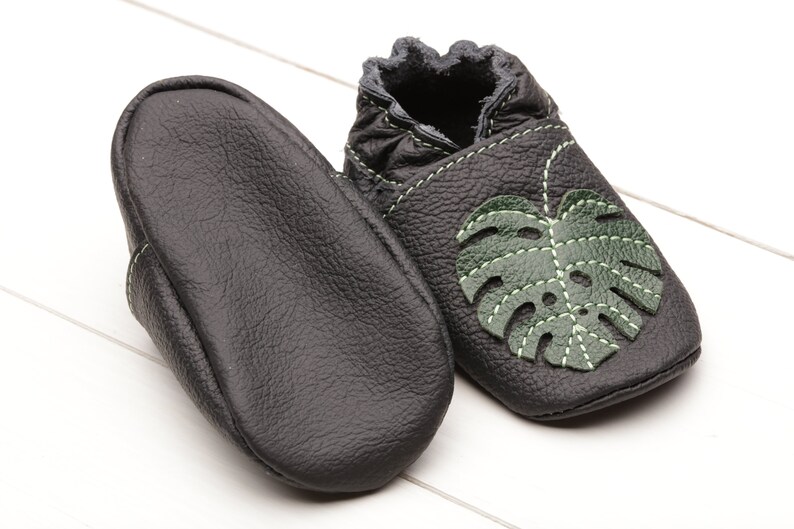May include: Black leather baby shoes with a green leaf design. The shoes have a soft, flexible sole and are perfect for crawling and walking.