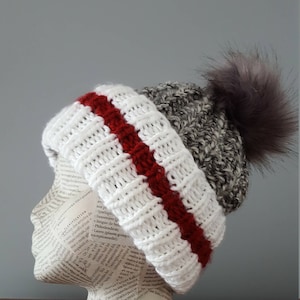 May include: White knit beanie with a red stripe and a gray pom pom. The beanie is on a mannequin head.
