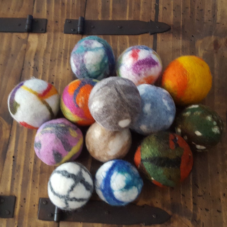 May include: A collection of 12 colorful wool dryer balls. The balls are made of felted wool and have various patterns and colors, including blue, green, orange, purple, and gray.