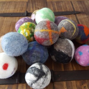 May include: A collection of colorful wool dryer balls in various patterns and colors, including blue, green, red, white, and purple. The balls are made of felted wool and are designed to help reduce drying time and soften laundry.