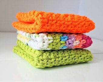 May include: A stack of four handmade crochet washcloths in vibrant colors. The top washcloth is bright orange, followed by a multi-colored one with pink, purple, and blue accents. The bottom two are lime green.