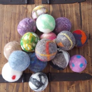 May include: A collection of 15 colorful felt balls in various patterns and colors, including green, blue, pink, purple, gray, and brown. The balls are arranged in a pile on a wooden surface.