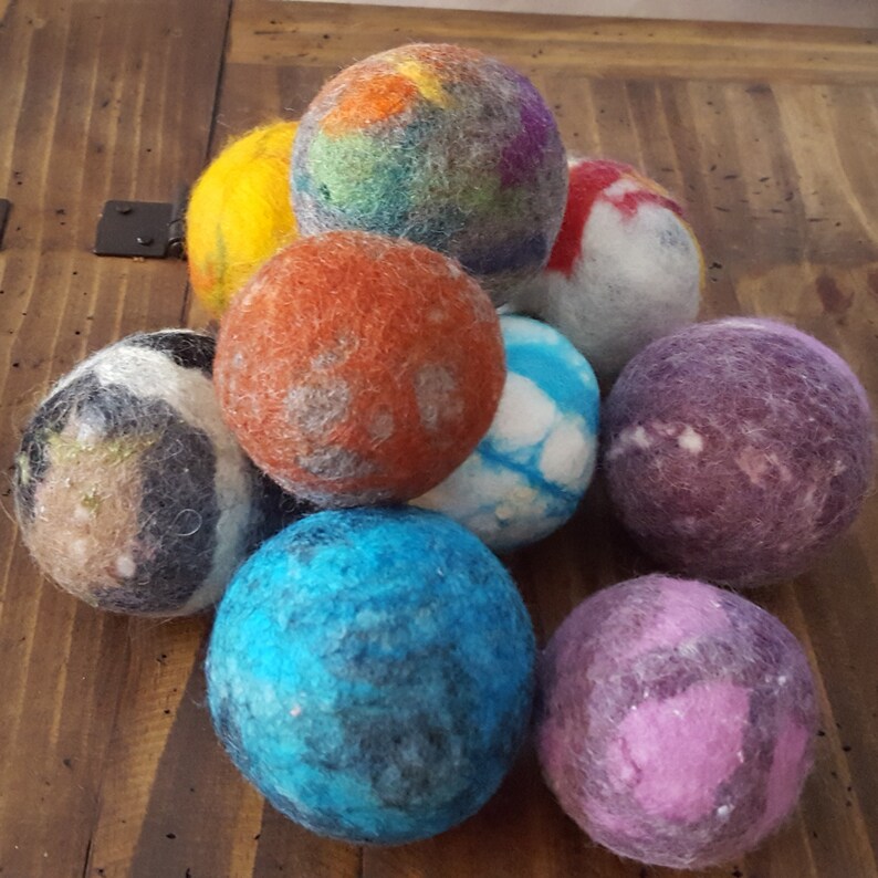 May include: A collection of nine colorful felted wool balls. The balls are various shades of blue, purple, orange, yellow, and white. The balls are arranged in a pyramid shape.