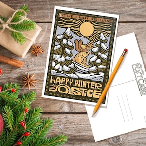 May include: A postcard with a winter scene featuring a rabbit in a snowy forest. The text on the postcard reads "The Light Returns" and "Happy Winter Solstice".