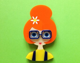 ISA Acrylic Brooch . Ginger Hair girl, wearing a hair bun, a flower in her red hair and blue glasses and a dungaree