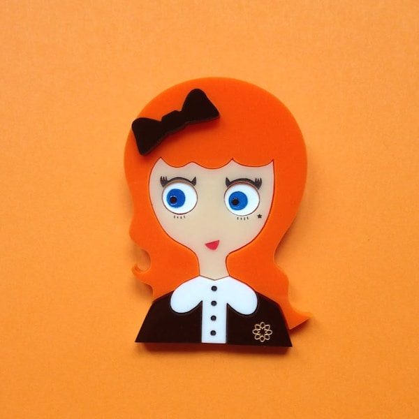 Broche acrylique KATHERINE. Jeune fille rousse avec noeud dans les cheveux, chemisier blanc et une broche dorée.