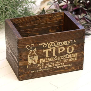 Puede incluir: Una caja de madera marrón oscuro con un diseño vintage. La caja tiene una etiqueta dorada con el texto "CALIFORNIA TIPO ITALIAN-SWISSCOLONY FERS OF LICICE CALIFORNIA WINES 51 BROADWAY SAN FRANCISCO CALIFORNIA".