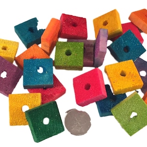 May include: A collection of colorful wooden squares with holes in the center. The squares are various shades of green, blue, purple, orange, yellow, and red. The squares are scattered on a white background.