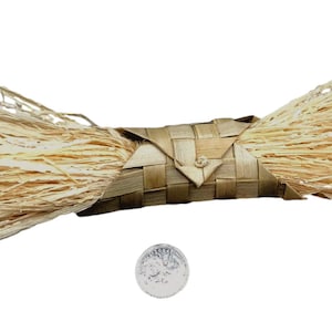 May include: A bundle of natural, light brown, shredded wood fibers wrapped in a woven, light brown, basket-like material. The bundle is about 6 inches long and 2 inches wide. A silver coin is placed below the bundle for scale.